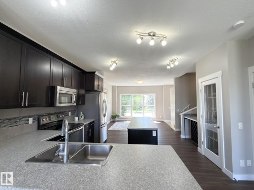 Kitchen featuring dark wood-finish cabinetry, stainless steel appliances, a double basin sink, and an island with built-in storage - 3110 Paisley Road, Edmonton, AB 