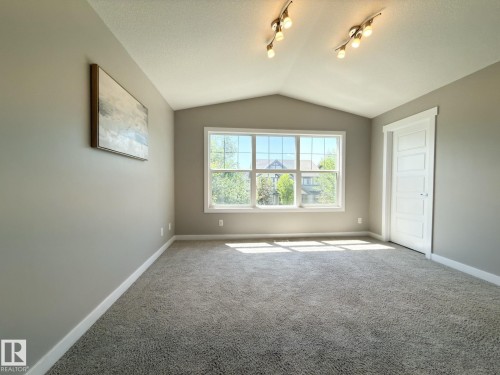 Room featuring vaulted ceilings with track lighting, grey carpeting, and a large window with white trim - 3110 Paisley Road, Edmonton, AB 