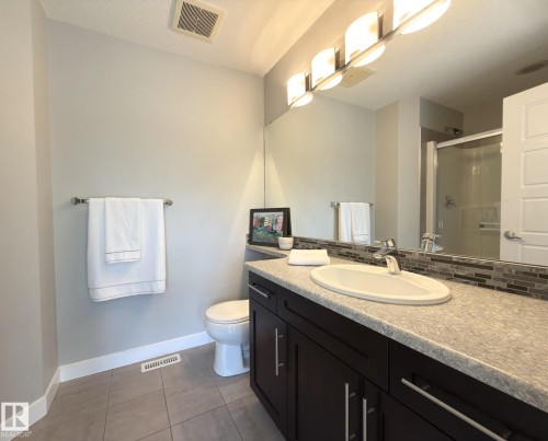 Bathroom featuring a dark wood-finish vanity with an integrated sink, a light-toned countertop, and a mosaic tile backsplash - 3110 Paisley Road, Edmonton, AB 