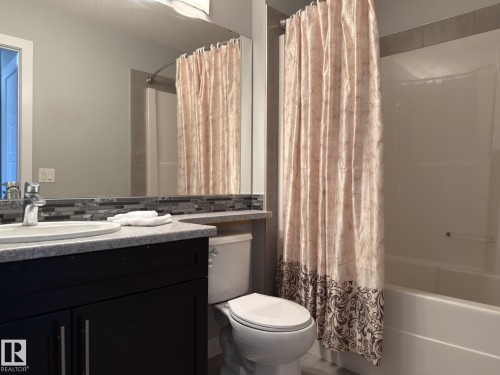 Bathroom featuring a dark wood-finish vanity with a light speckled countertop, rectangular undermount sink, and mosaic tile backsplash - 3110 Paisley Road, Edmonton, AB 