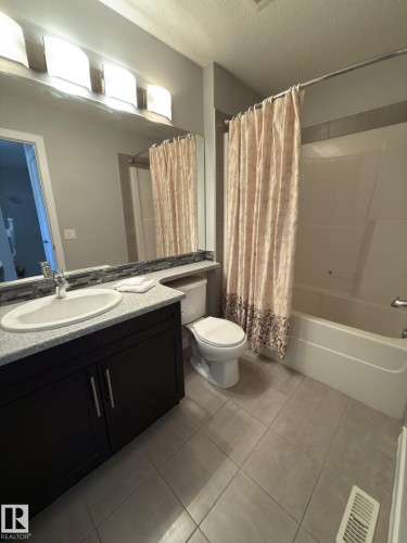 Bathroom featuring a dark wood-finish vanity with a light speckled countertop, an undermount sink, a large wall mirror, and a white bathtub with a shower - 3110 Paisley Road, Edmonton, AB 