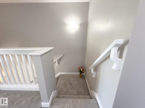 Carpeted staircase with white balusters and handrails, featuring light gray wall paint and a wall-mounted light fixture - 3110 Paisley Road, Edmonton, AB 