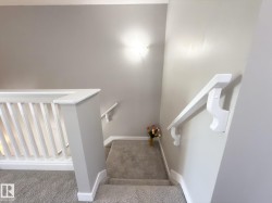 Carpeted staircase with white balusters and handrails, featuring light gray wall paint and a wall-mounted light fixture - 