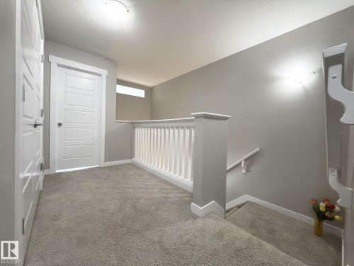 Upper-level hallway featuring neutral-toned carpeting, white baluster railing, white paneled doors, and a translucent transom window - 3110 Paisley Road, Edmonton, AB 