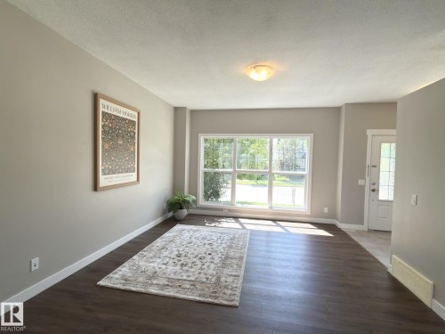 Spacious living area featuring wood-finish flooring, neutral wall tones, and a large picture window - 3110 Paisley Road, Edmonton, AB 