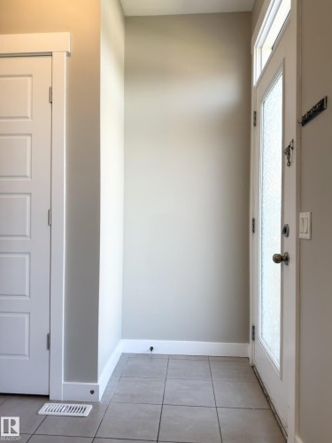 Entryway featuring square tile flooring, a white paneled door with contemporary hardware, and a white front door with frosted glass and transom window - 3110 Paisley Road, Edmonton, AB 