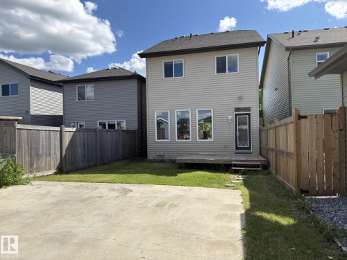 Rear exterior featuring a ground-level wood deck, a rear entry door with a full-lite insert, horizontal siding, and multiple windows - 3110 Paisley Road, Edmonton, AB 