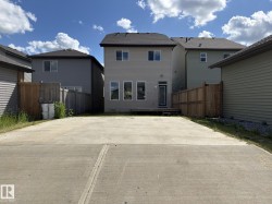 Rear exterior featuring light beige siding, a black shingle roof, and a concrete patio - 