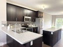 Kitchen featuring dark wood-finish cabinetry, light-toned countertops, a stainless steel double-basin sink, and a tile backsplash with mosaic accents - 3110 Paisley Road, Edmonton, AB 