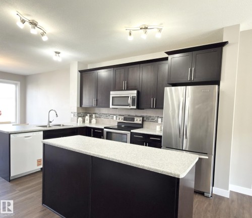 Modern kitchen featuring dark wood-finish cabinetry, light speckled countertops, and stainless steel appliances - 3110 Paisley Road, Edmonton, AB 