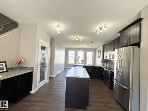 Open-concept kitchen featuring dark wood cabinetry, stainless steel appliances, a center island with a light-toned countertop, and wood-finish flooring - 3110 Paisley Road, Edmonton, AB 