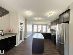 Open-concept kitchen featuring dark wood cabinetry, stainless steel appliances, a center island with a light-toned countertop, and wood-finish flooring - 