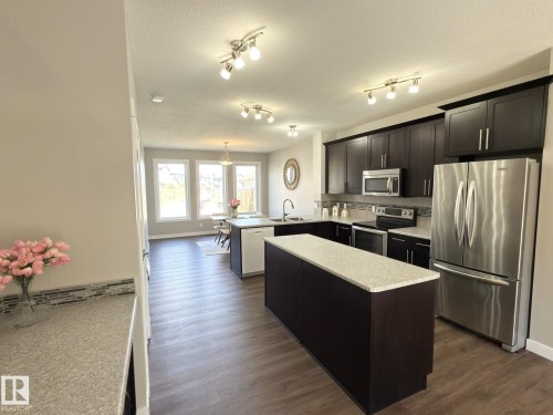 Kitchen featuring dark wood cabinetry, stainless steel appliances, a center island with light-toned countertop, and wood-finish flooring - 3110 Paisley Road, Edmonton, AB 