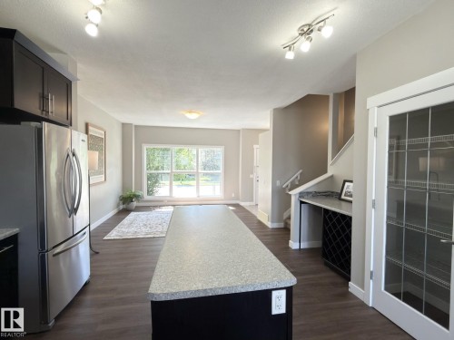 Open concept living space featuring wood-finish flooring, a kitchen island with a light-colored countertop, and a stainless steel refrigerator - 3110 Paisley Road, Edmonton, AB 
