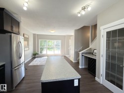Open concept living space featuring wood-finish flooring, a kitchen island with a light-colored countertop, and a stainless steel refrigerator - 