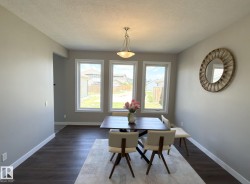 Dining area featuring three large windows with white trim, dark wood-finish flooring, light grey painted walls, and a ceiling-mounted light fixture - 