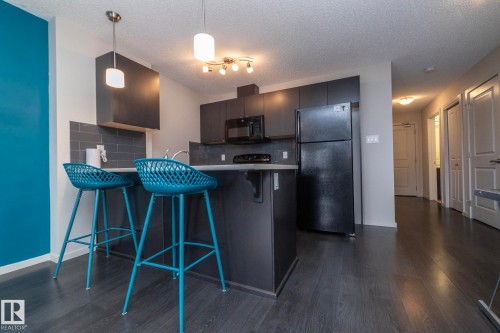 Modern kitchen featuring dark wood-finish flooring, dark cabinetry, and a black appliance suite including a refrigerator and microwave - 431 344 Windermere Road, Edmonton, AB - Indoor Photo Showing Kitchen