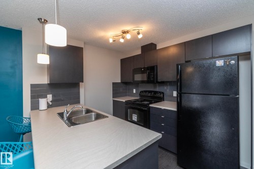 Modern kitchen featuring dark cabinetry, light countertops, and a subway tile backsplash - 431 344 Windermere Road, Edmonton, AB - Indoor Photo Showing Kitchen With Double Sink