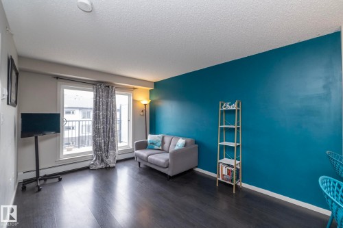 Living area featuring a sliding glass door to a balcony, dark wood-finish flooring, and a vibrant accent wall - 431 344 Windermere Road, Edmonton, AB - Indoor