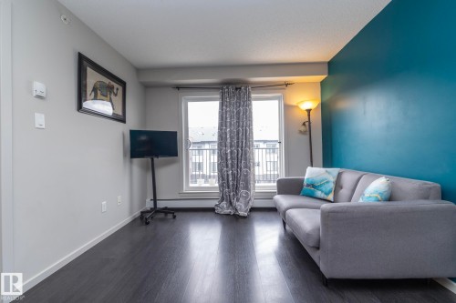 Spacious room featuring dark wood-finish flooring, a full wall of vibrant blue paint, and light gray walls - 431 344 Windermere Road, Edmonton, AB - Indoor Photo Showing Living Room