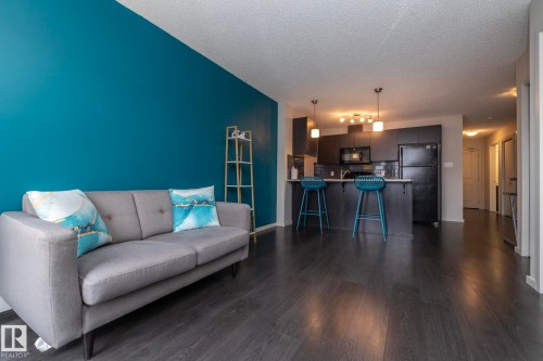 Open-concept living space featuring dark wood-finish flooring, a vibrant accent wall, and a kitchen with dark cabinetry - 431 344 Windermere Road, Edmonton, AB - Indoor Photo Showing Living Room