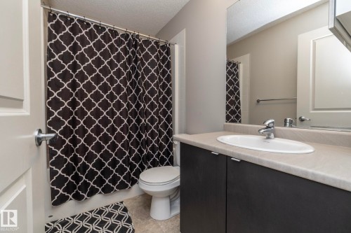 Bathroom featuring a vanity with dark wood-finish cabinetry, a light-toned countertop, and an integrated oval sink with a chrome faucet - 431 344 Windermere Road, Edmonton, AB - Indoor Photo Showing Bathroom