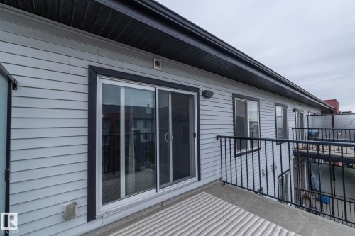 Private balcony featuring a sliding glass door, light gray siding, black metal railings, and a dark soffit - 431 344 Windermere Road, Edmonton, AB - Outdoor With Deck Patio Veranda With Exterior