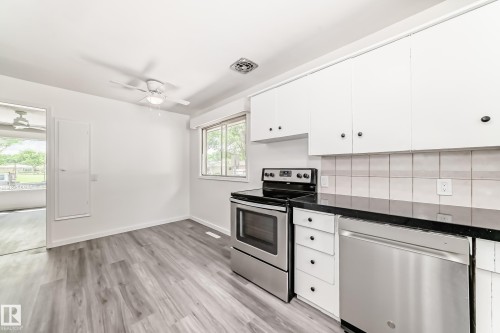 Kitchen featuring stainless steel appliances, dark countertops, white cabinetry, and wood-finish flooring - 11937 39 Street Nw, Edmonton, AB 