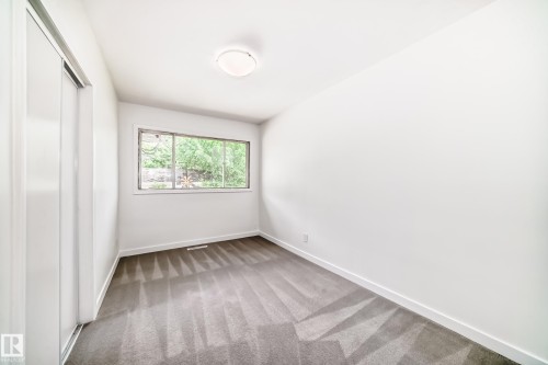 Bright room featuring a window with green foliage visible, light gray carpeting, crisp white walls, and a recessed ceiling light fixture - 11937 39 Street Nw, Edmonton, AB 