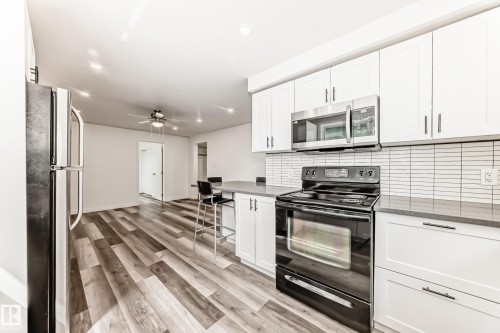 Modern kitchen featuring white shaker cabinetry, stainless steel microwave, black electric range, and gray countertops - 11937 39 Street Nw, Edmonton, AB 