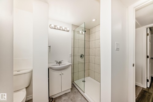 Bathroom featuring a walk-in shower with glass enclosure, white tile surround, and built-in vanity with basin sink - 11937 39 Street Nw, Edmonton, AB 