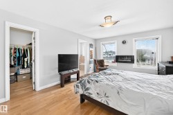 Bedroom featuring wood-finish flooring, two windows with white trim, a built-in wall-mounted fireplace, and a ceiling-mounted light fixture - 
