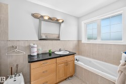 Bathroom featuring a single vanity with wood cabinetry and a dark countertop, an integrated drop-in sink, and a rectangular mirror with an overhead light fixture - 