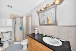 Bathroom featuring a wood-finish vanity with a dark countertop and integrated sink, a glass-enclosed shower, and a white toilet - 