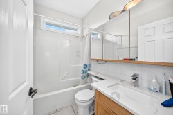 Bright bathroom featuring a tub-shower combination with a transom window, a wood-finish vanity with an integrated sink, a mirrored medicine cabinet, and overhead lighting - 