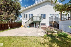 Rear exterior featuring two levels of windows, two sets of exterior stairs, a raised garden bed, and a concrete patio surface - 