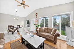 Vaulted ceiling living space featuring hardwood flooring, abundant natural light from large windows, and an overhead ceiling fan - 