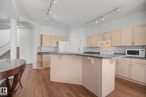 Spacious kitchen featuring light wood cabinetry, dark countertops, a large island with a breakfast bar, and track lighting - 262 Dunvegan Road, Edmonton, AB 