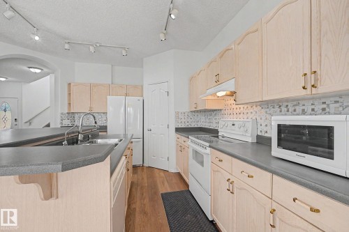 Kitchen featuring light wood-finish cabinetry, dark countertops, and a mosaic tile backsplash - 262 Dunvegan Road, Edmonton, AB 