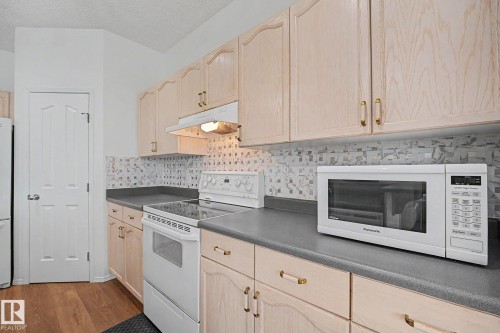 Kitchen featuring light wood-finish cabinetry, solid surface countertops, mosaic tile backsplash, and wood-finish flooring - 262 Dunvegan Road, Edmonton, AB 