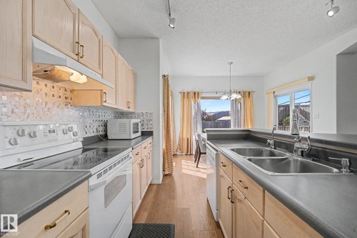 Kitchen featuring light wood cabinetry, white appliances, a mosaic tile backsplash, and wood-finish flooring - 262 Dunvegan Road, Edmonton, AB 