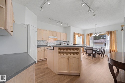 Kitchen featuring wood-finish cabinetry, a central island with integrated wine storage, grey countertops, and a full suite of appliances - 262 Dunvegan Road, Edmonton, AB 
