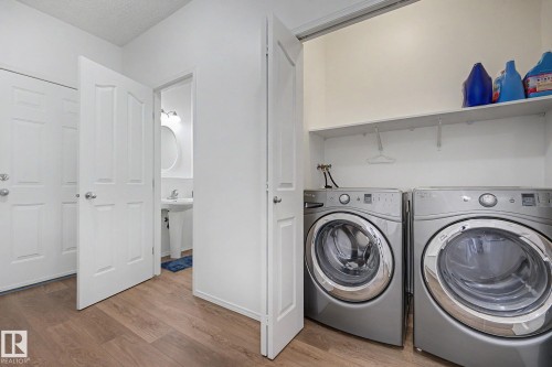 Dedicated laundry area featuring front-loading washer and dryer units, overhead shelving, and wood-finish flooring - 262 Dunvegan Road, Edmonton, AB 