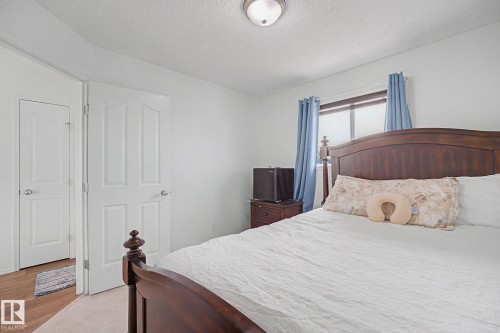 Carpeted bedroom featuring a window with blue curtains, a ceiling-mounted light fixture, and two panel doors - 262 Dunvegan Road, Edmonton, AB 