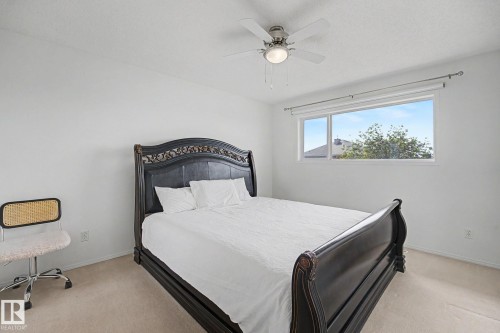 Bright bedroom featuring a large window, neutral carpet flooring, a ceiling fan with integrated lighting, and white walls - 262 Dunvegan Road, Edmonton, AB 