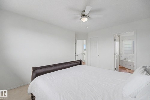 Carpeted bedroom featuring a ceiling fan with integrated lighting, white walls, and a white paneled door - 262 Dunvegan Road, Edmonton, AB 
