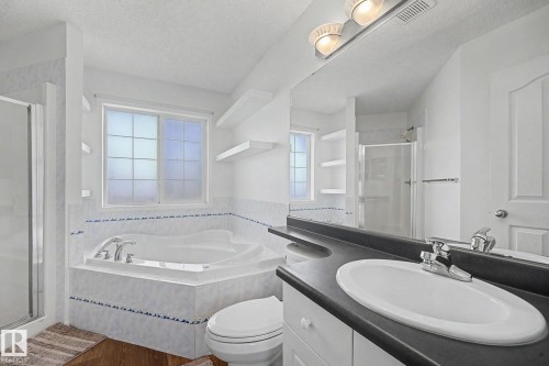 Bathroom featuring a built-in corner soaking tub with tiled surround, a separate glass-enclosed shower, and a vanity with an integrated sink and dark countertop - 262 Dunvegan Road, Edmonton, AB 
