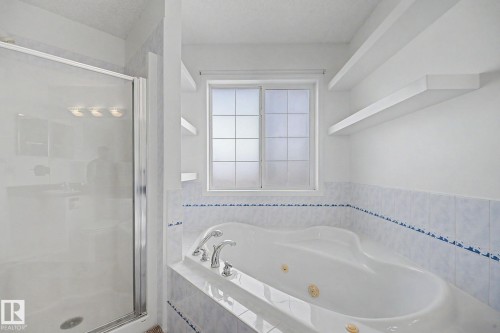 Spacious bathroom featuring a built-in jetted tub with chrome fixtures, a frosted window, and two floating wall shelves - 262 Dunvegan Road, Edmonton, AB 