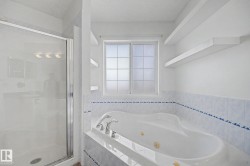 Spacious bathroom featuring a built-in jetted tub with chrome fixtures, a frosted window, and two floating wall shelves - 