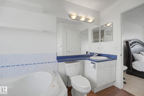 Bathroom featuring a built-in tub, white toilet, and a vanity with a white basin sink and blue countertop - 262 Dunvegan Road, Edmonton, AB 